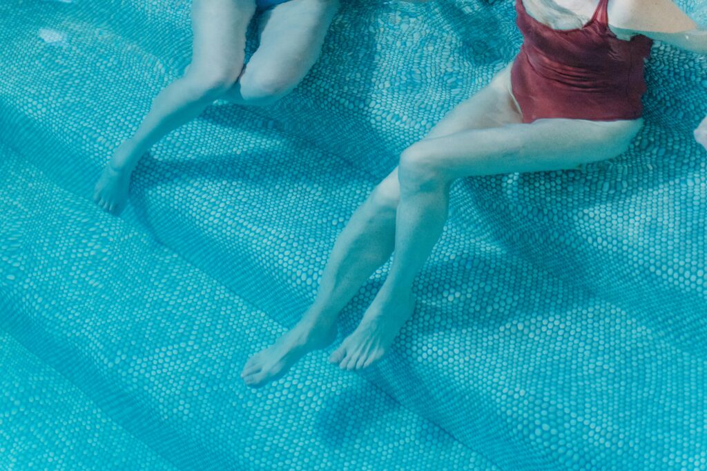 Two people in swimsuits lounging in a clear blue swimming pool, relaxing under the sun.